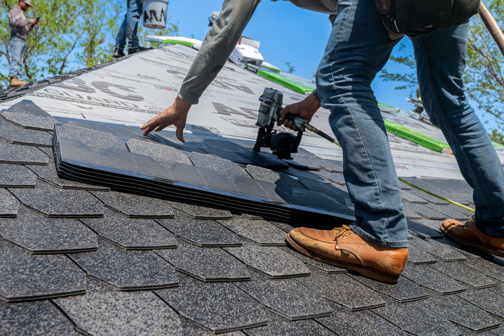 Roofer nailing down architectural shingles on a residential roof