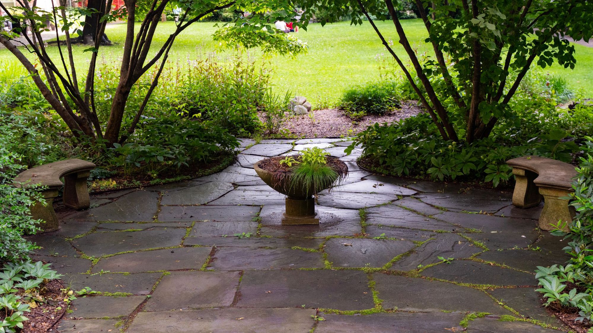 Flagstone courtyard with stone benches and a planted urn under trees