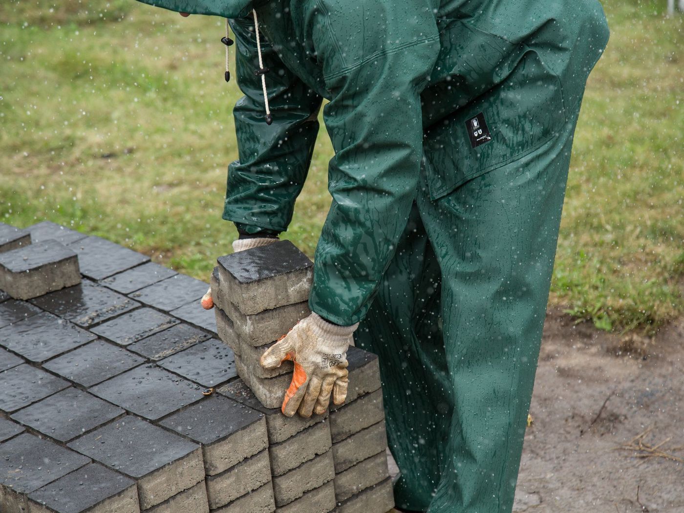 Gloved hands setting a paver into a sand bed