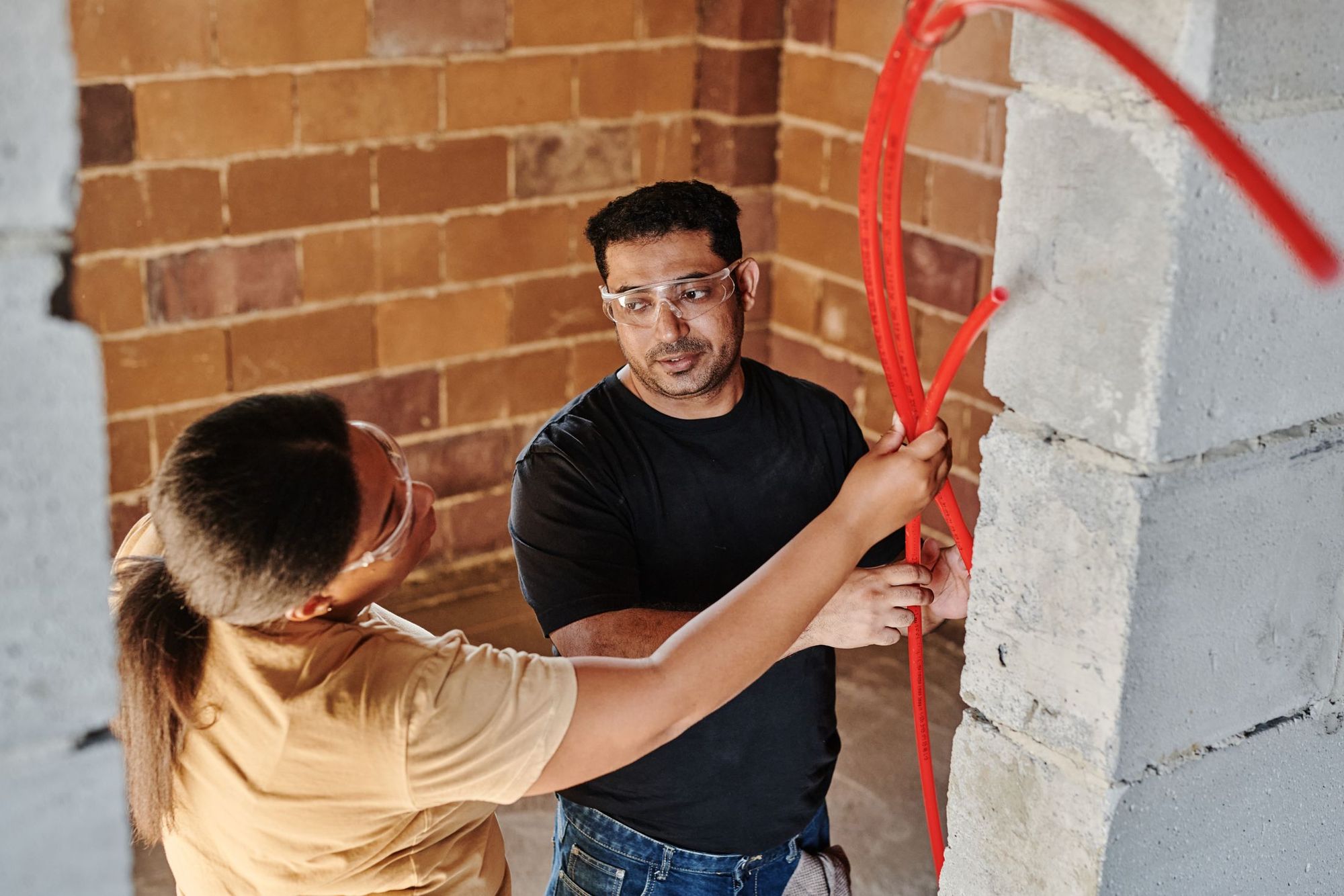 Two plumbers fitting PEX supply line along a brick wall