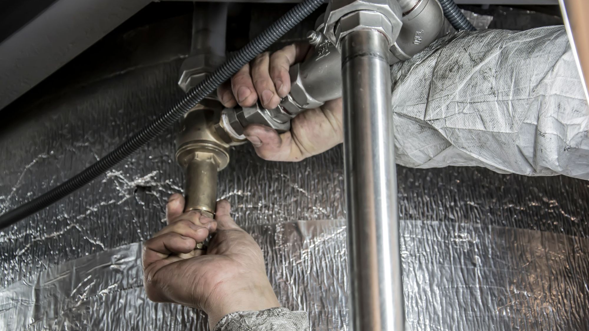 Plumber's hands tightening a fitting on a supply line under a sink