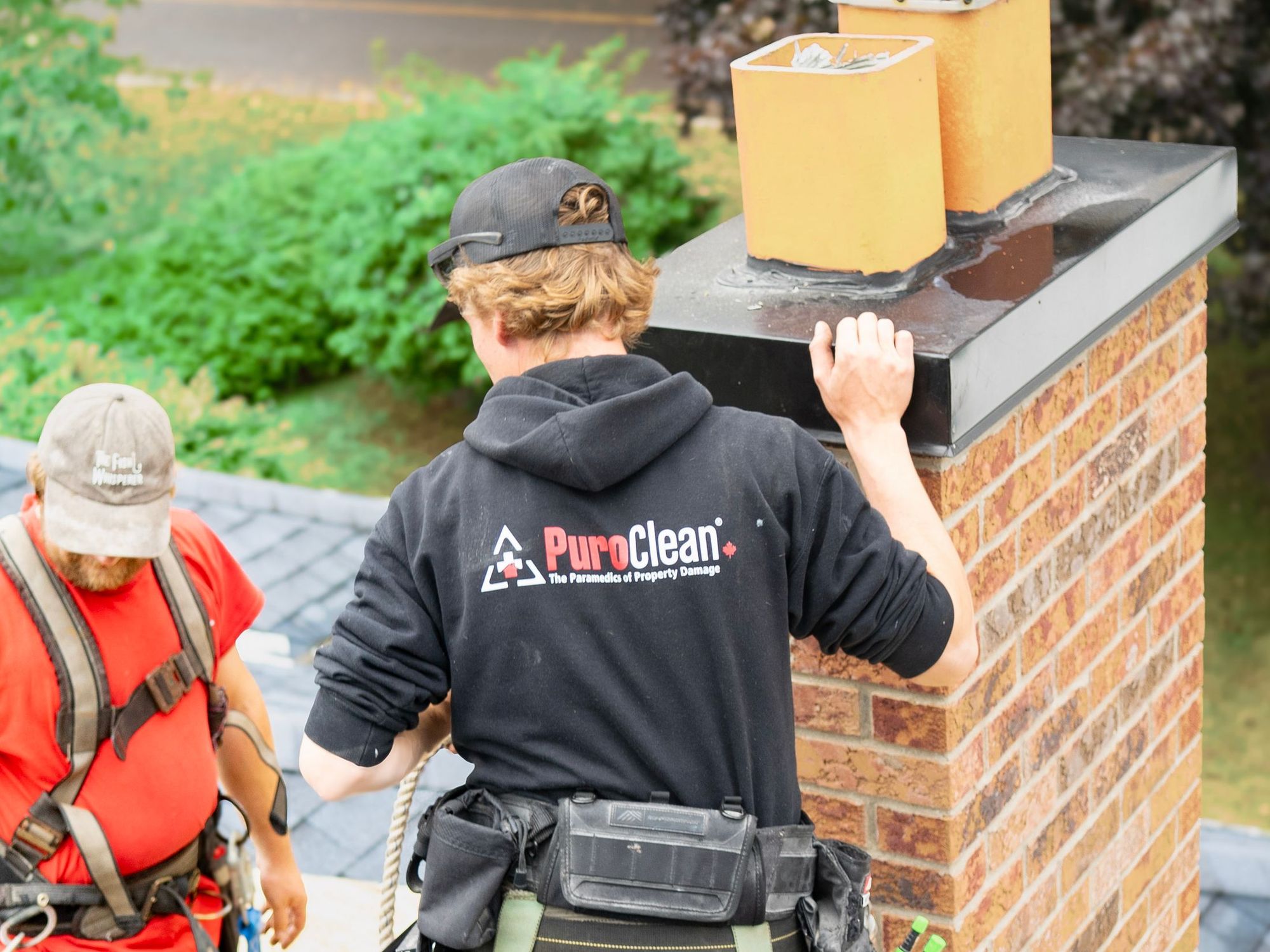 Two roofers at a brick chimney checking the counter flashing
