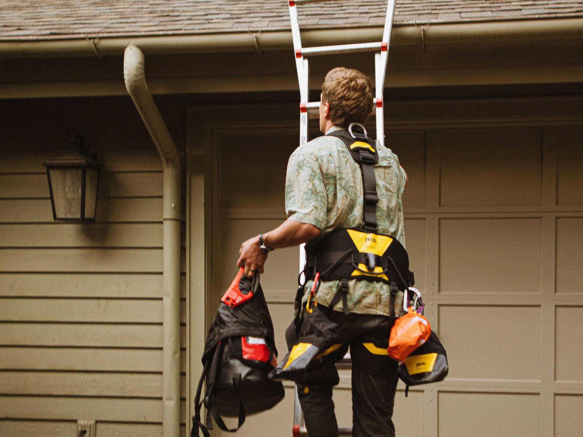 Roofer climbing a ladder to a garage roof in the late afternoon