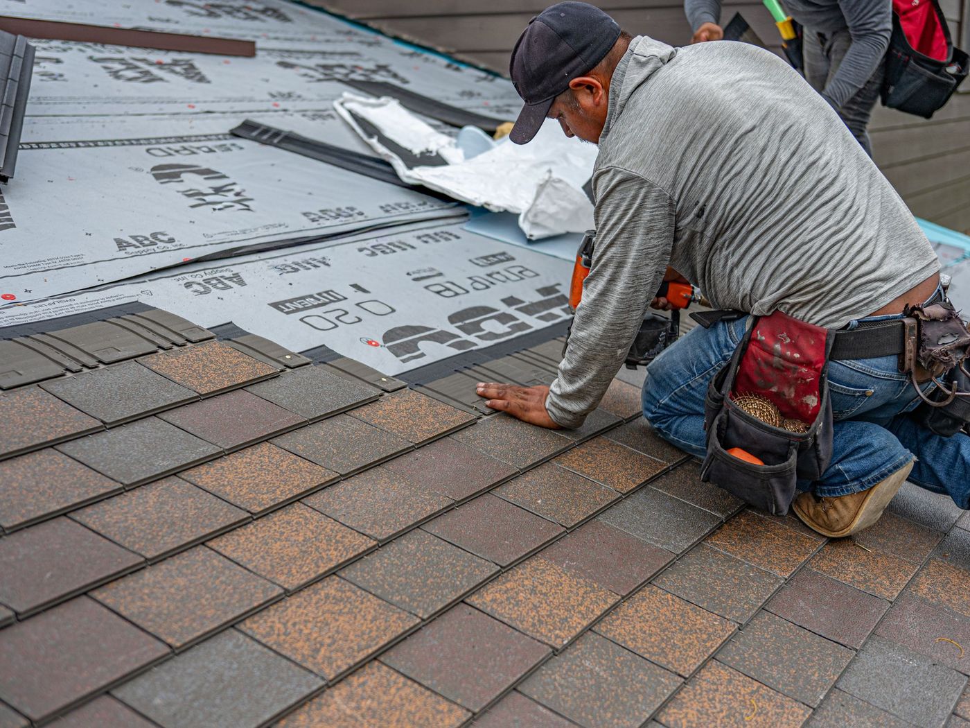 Roofer kneeling on a damaged section of shingle roof