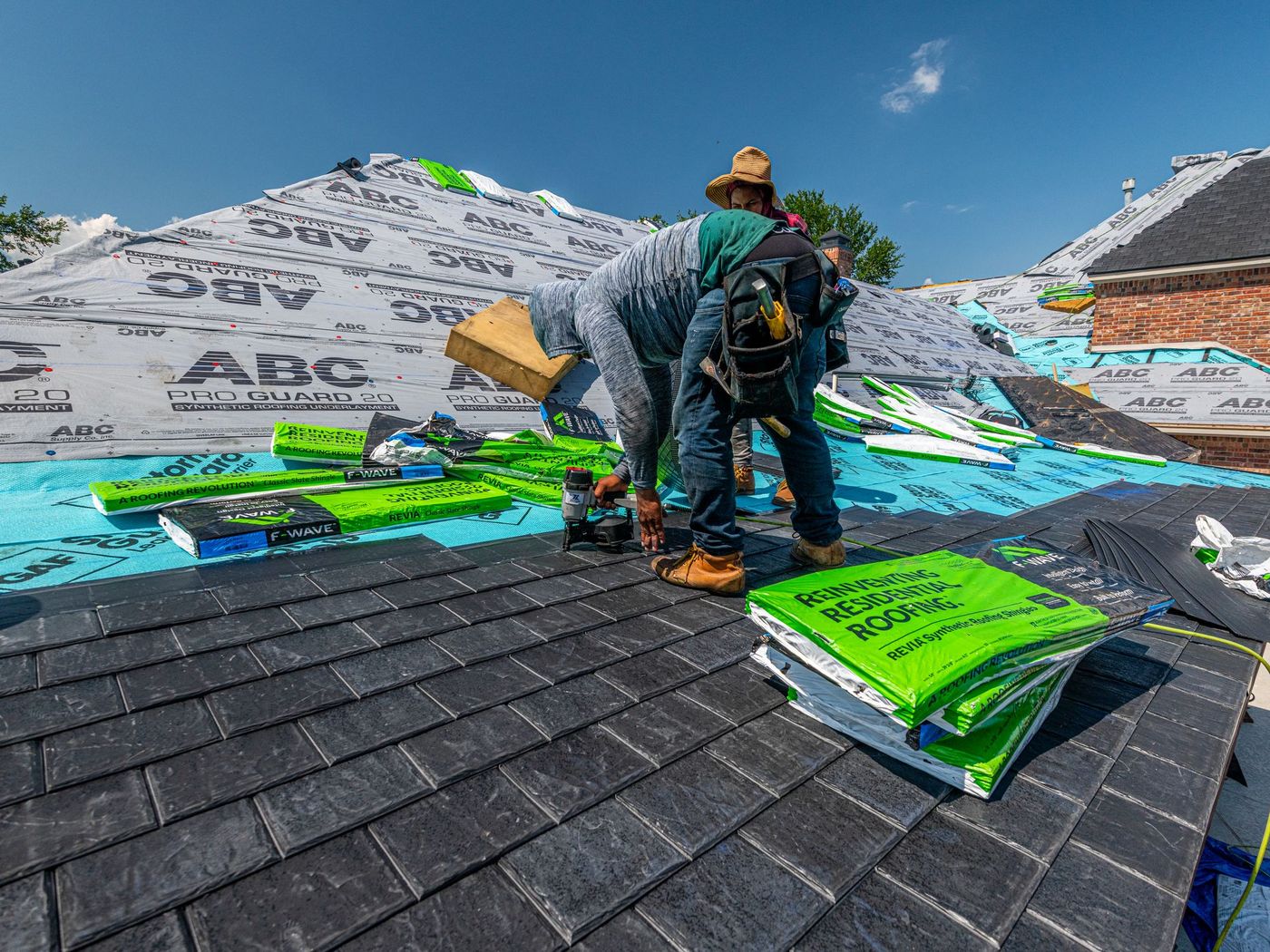 Roofers laying underlayment and shingles on a steep roof